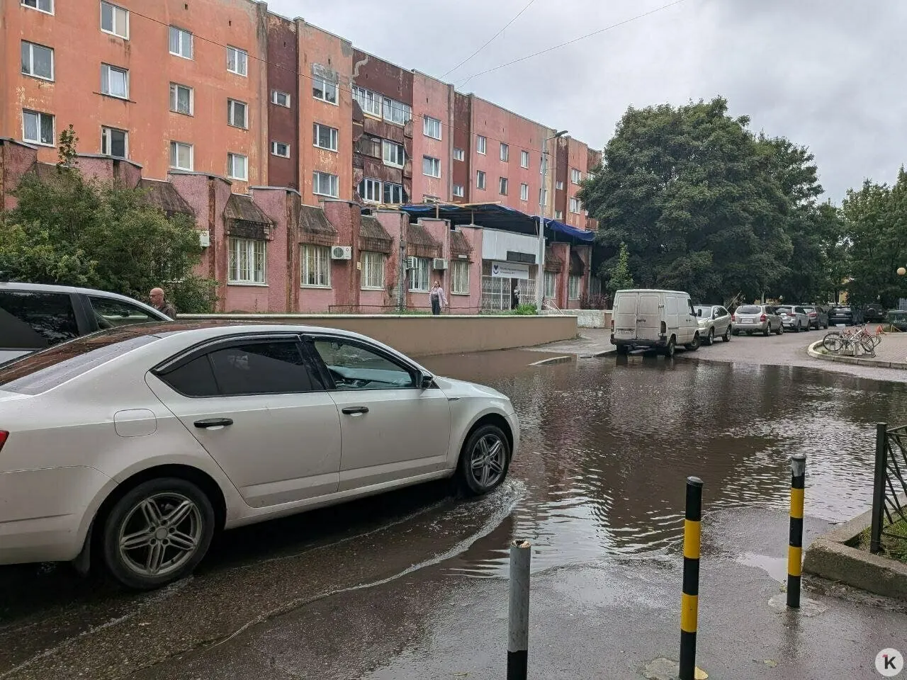 Сильный дождь затопил подход к поликлинике: лужа у крыльца такая глубока, что пройти её вброд невозможно, а люди вынуждены обходить лужу по газону и перелезать через забор.